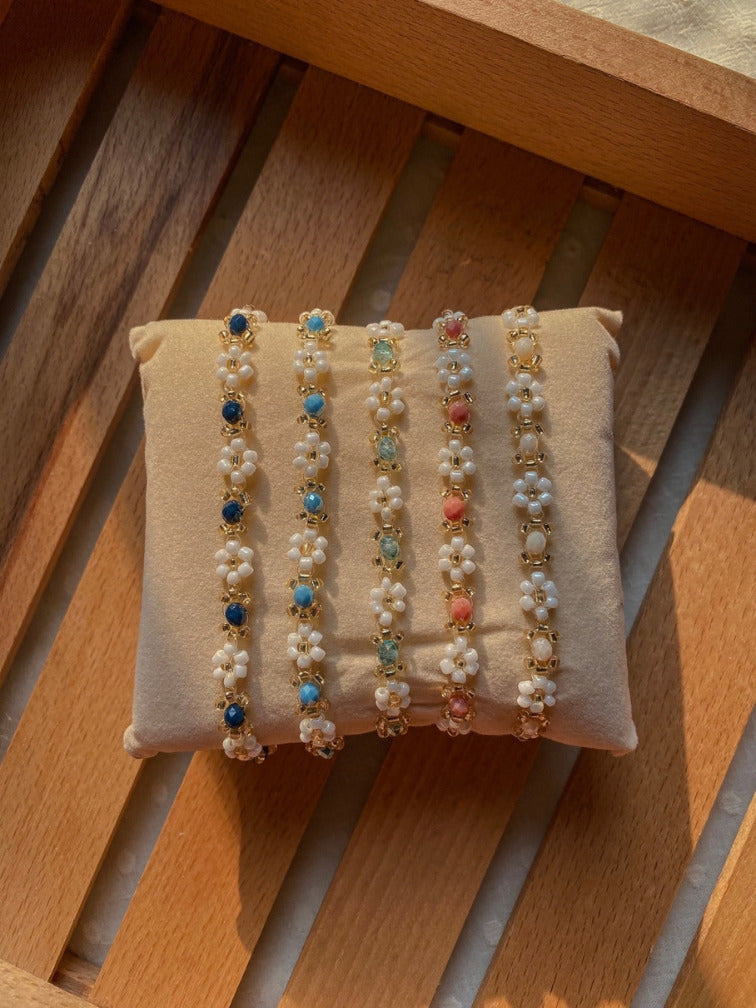 Five dainty stackable daisy bracelets displayed on beige velvet jewelry cushion