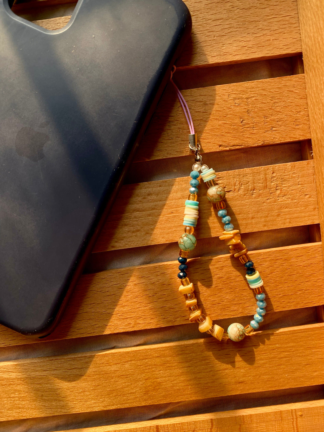 Beaded phone charm on a wooden surface with a black phone case.