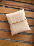 A beaded bracelet with white daisy flowers and coral-pink centers, accented with gold-toned metal, displayed on a beige fabric pillow over a wooden slatted surface.
