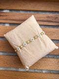 A beige fabric jewelry pillow displaying a Creamy Off-White Daisy Beaded Bracelet, resting on a wooden slatted surface.
