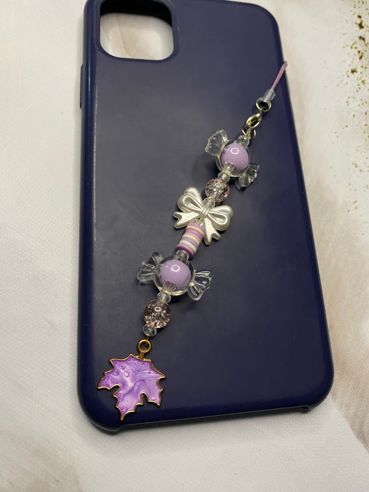 Purple enamel maple leaf charm with gold rim hanging from phone strap
