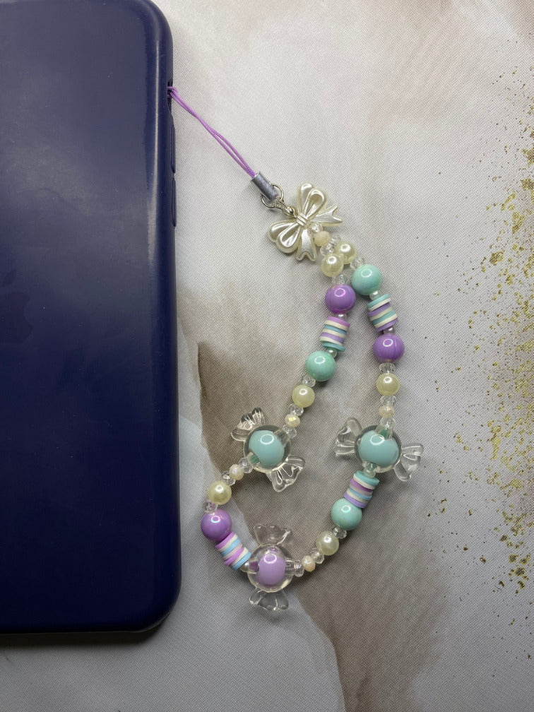 Close-up of clear candy charm beads with silver bow on phone strap