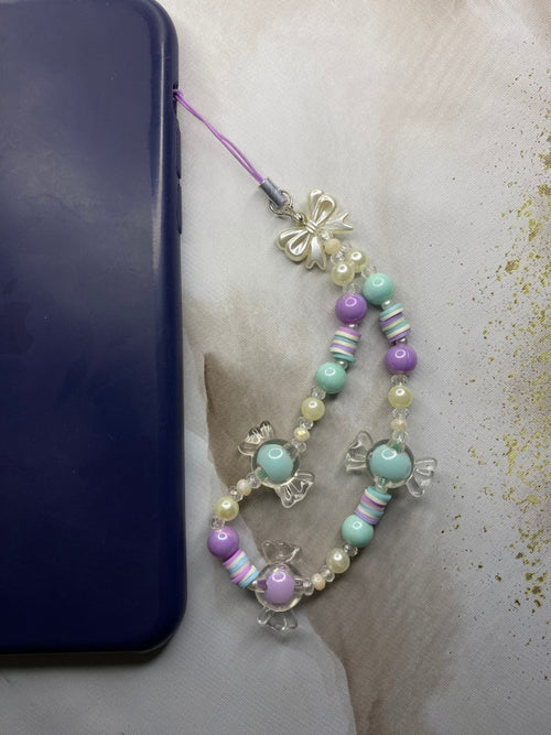Close-up of clear candy charm beads with silver bow on phone strap