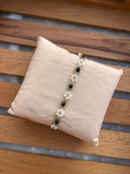 A bracelet with white faux pearls and dark navy oval stones, displayed on a beige fabric pillow over a wooden slatted surface.