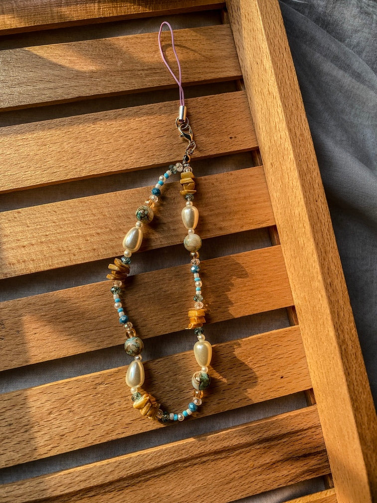 Pearl phone charm with purple cord on wooden background