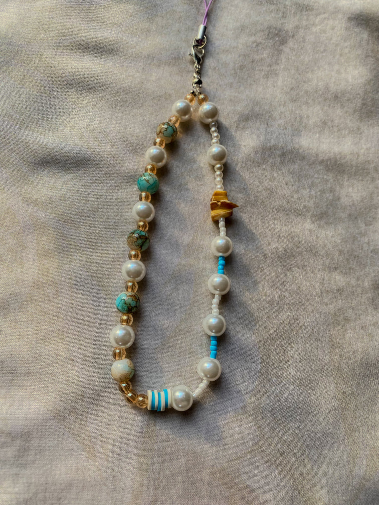 Beaded phone charm with pearls, turquoise, and gold beads on a textured surface