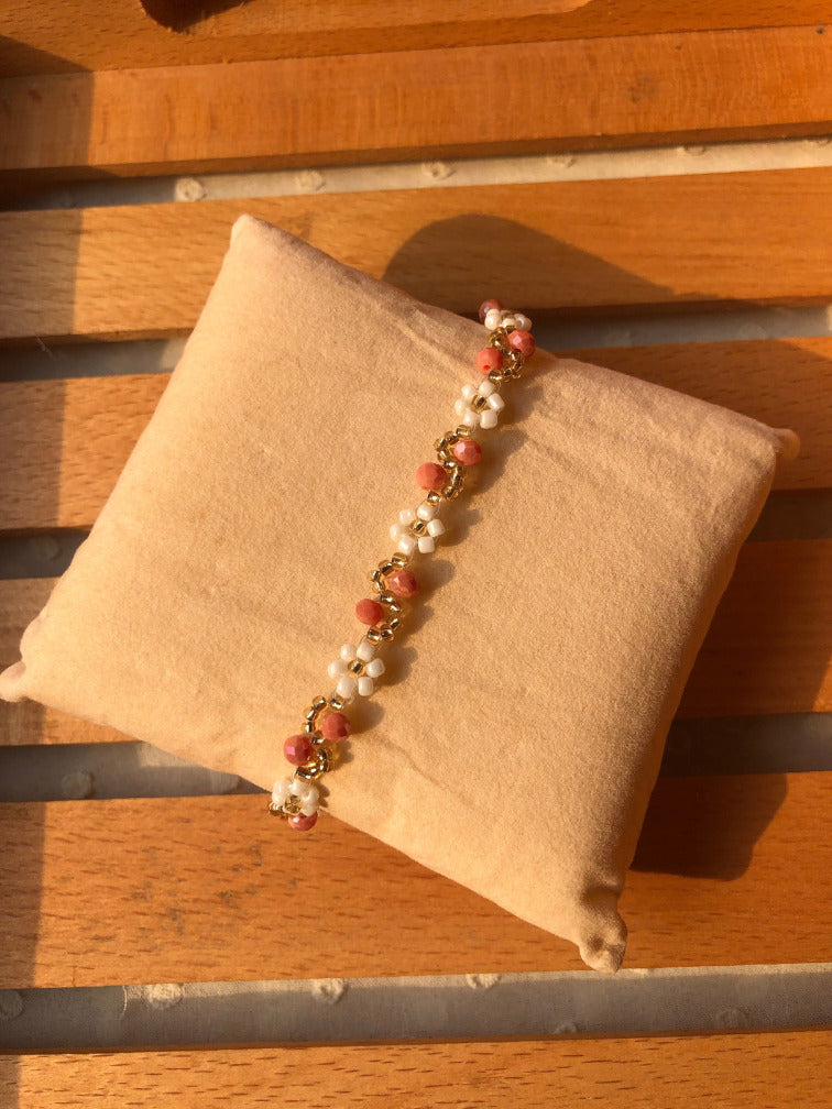 Handmade white daisy and coral pink faceted bead bracelet with gold accents on cream cushion
